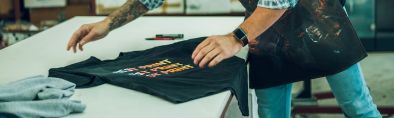 Person screen-printing a custom graphic T-shirt on a worktable in an apparel printing studio.